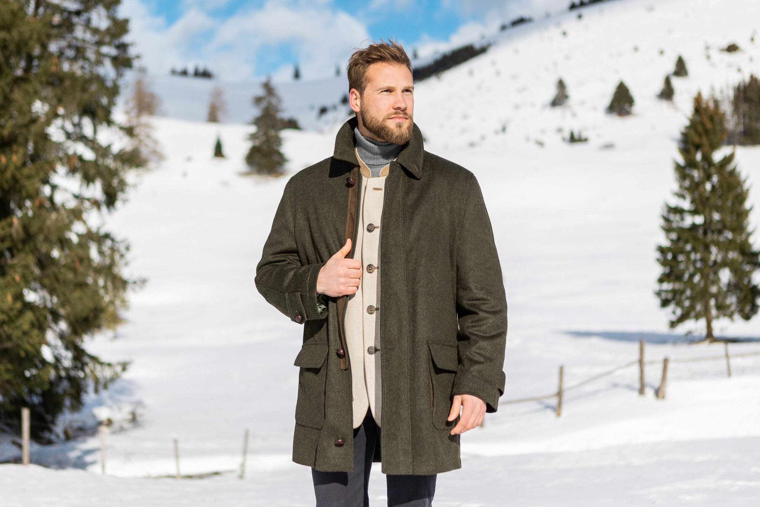 Young man wearing a Loden wool field coat from Robert W. Stolz over a tyrolean jacket in a snowy mountain setting